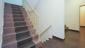 Una escalera con baldosas de tonos marrones oscuros y claros, paredes blancas y barandilla de madera.