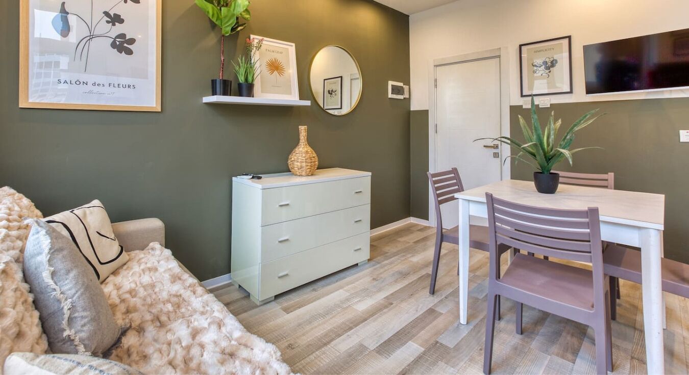 Un salon moderne avec un canapé, une table à manger et des chaises, une commode blanche et un miroir.