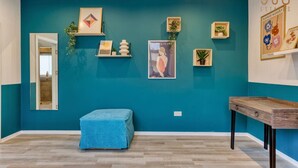 A room with teal walls, a blue bench, a wooden table, and various framed artworks.