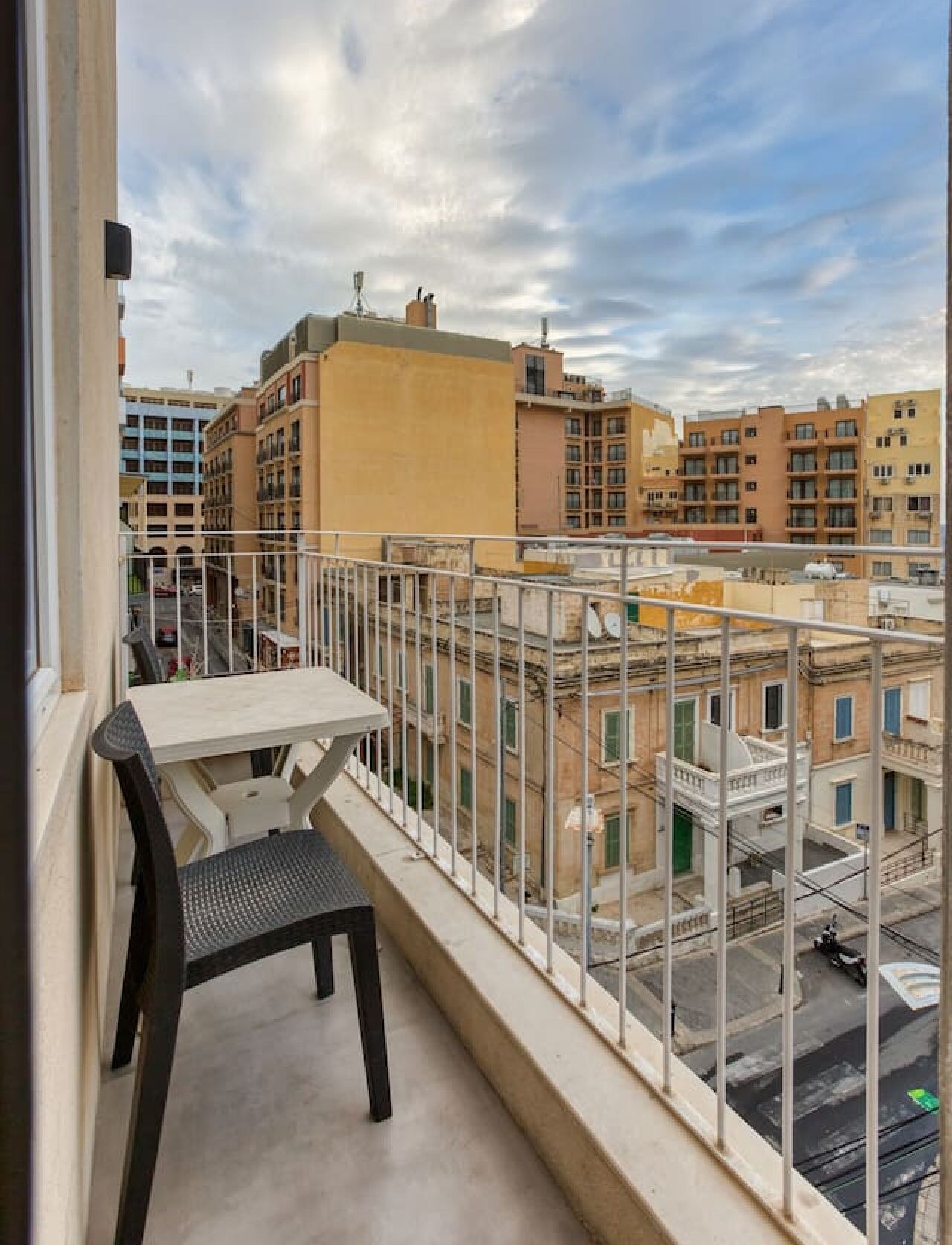 Un balcón con mesa y silla, con vistas a un paisaje urbano con edificios de varios pisos.