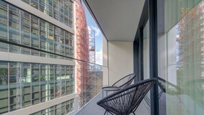 Een balkon met twee zwarte metalen stoelen, grote ramen en uitzicht op een gebouw in aanbouw.