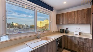 Une cuisine moderne avec des meubles en bois, un lave-linge encastré et une grande fenêtre donnant sur le paysage urbain.