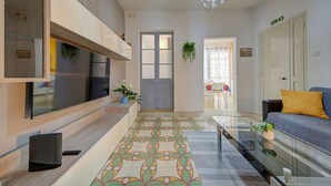 Una sala de estar moderna con un televisor grande, una mesa de centro de vidrio y un sofá con un cojín amarillo.