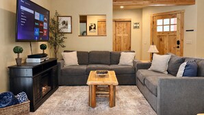 Una sala moderna con un sofá gris, una mesa de centro de madera y un televisor de pantalla plana montado en la pared.