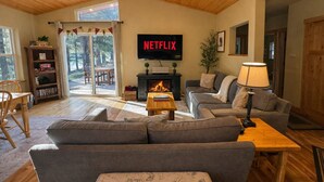 Un salón acogedor con chimenea, un sofá, un televisor mostrando 'NETFLIX' y una estantería.