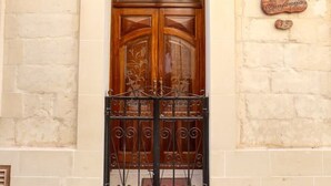 A beige building with a wooden double door, a wrought iron gate, and a street lamp.