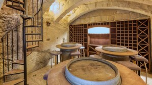 A stone-walled room with a spiral staircase, wooden tables with round tops, and a grid-like wooden partition.