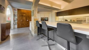 A modern kitchen with a central island, bar stools, and a stone column. - Stunning Villa with private pool & large terrace! (Balzan)
