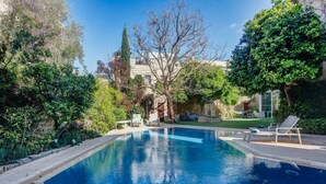 A rectangular swimming pool with clear blue water, surrounded by lush greenery and trees. There are lounge chairs and a hammock on the right side of the pool. - Stunning Villa with private pool & large terrace! (Balzan)