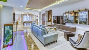 A modern living room with a sectional sofa, a glass coffee table, a TV, and decorative shelves. - 2BR Home in Mosta with Terrace & Vineyards View! (Il-Mosta)