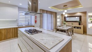 A modern kitchen with a central island, a dining area with a table and chairs, and a living area with a sofa and a TV. - 2BR Home in Mosta with Terrace & Vineyards View! (Il-Mosta)