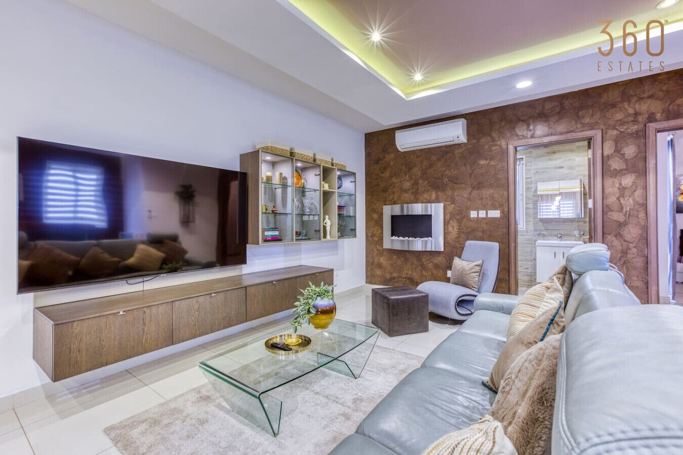 Un salon moderne doté d’un téléviseur à écran plat, d’une table basse en verre, d’un canapé en cuir et d’un mur décoratif en pierre.