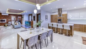 A modern kitchen with a central island, a dining area with a marble table, and a living room with a sofa and a TV. - 2BR Home in Mosta with Terrace & Vineyards View! (Il-Mosta)