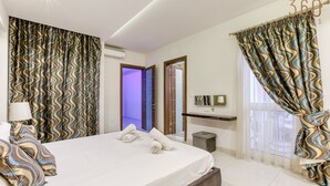 A modern hotel room with a large bed, a bedside table, a mirror, and a view of the outside. - 2BR Home in Mosta with Terrace & Vineyards View! (Il-Mosta)
