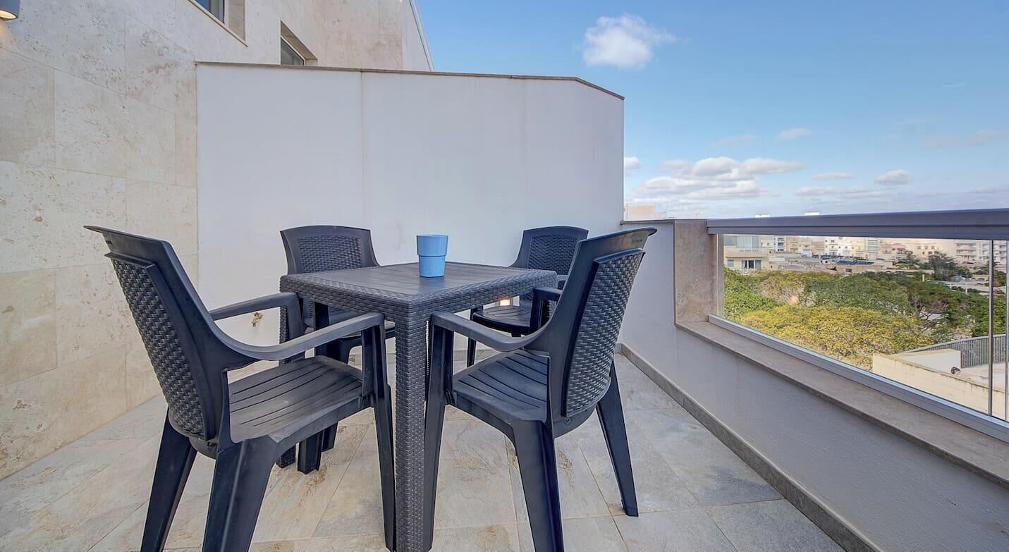 A balcony with a table and chairs, a view of the city, and a building in the background.