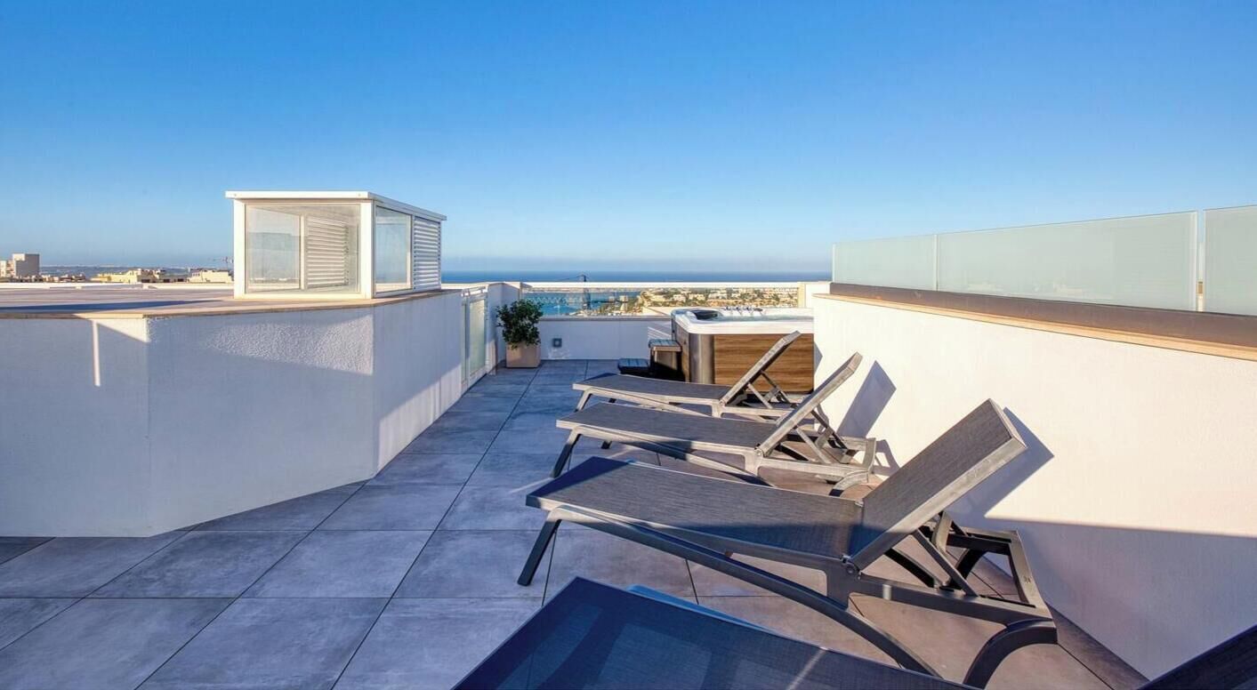 A rooftop terrace with sun loungers, a small table, and a glass enclosure.