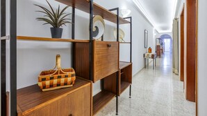 A hallway with a wooden cabinet, shelves with decorative items, and a potted plant.