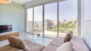 Ein modernes Wohnzimmer mit einem großen Schiebeglastür, die auf einen Balkon mit Blick auf die Stadt führt.