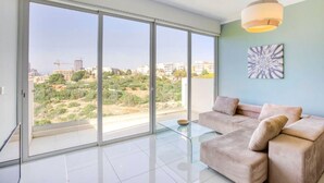 Ein geräumiges Wohnzimmer mit einem großen Schiebeglasfenster zum Balkon, ein beiges Sofa und eine moderne Leuchte.
