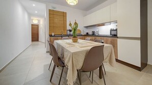A modern dining area with a table set for four, a kitchen in the background, and a hallway leading to a door.