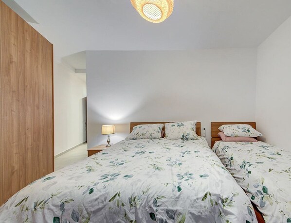 A bedroom with two beds, a wooden wardrobe, a bedside table with a lamp, and a ceiling light fixture. - Modern & Spacious 2BR Apt with Balconies  in Msida (L-Imsida)