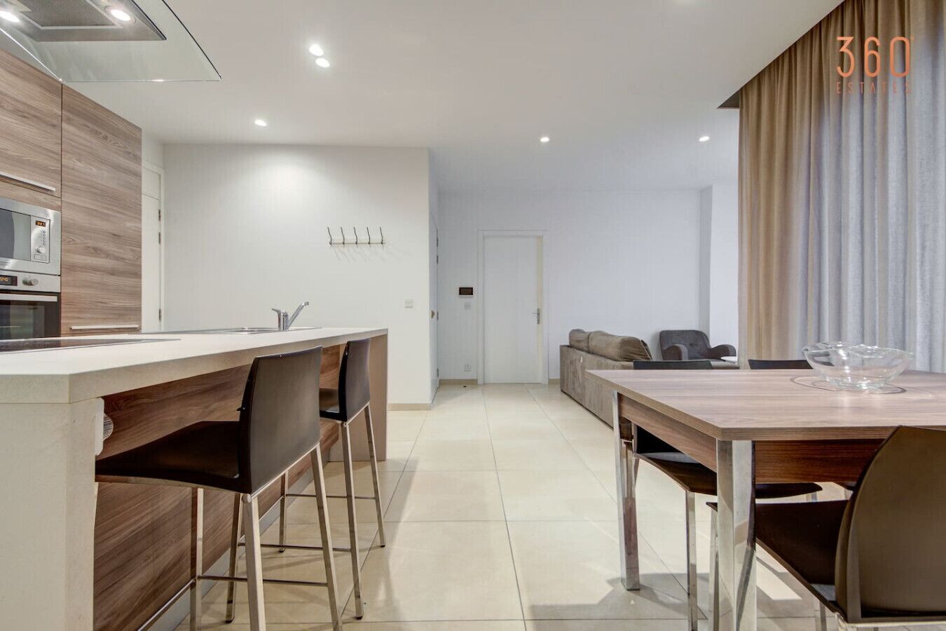 Een moderne keuken met een centraal eiland, een eethoek met een houten tafel en een woonruimte met een bank en stoelen.