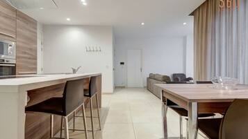 Een moderne keuken met een centraal eiland, een eethoek met een houten tafel en een woonruimte met een bank en stoelen.