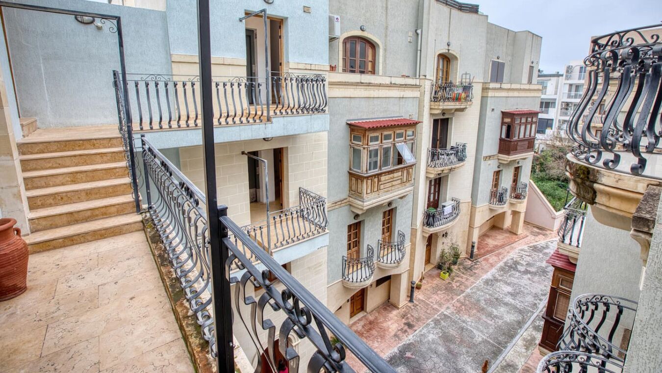 A multi-story residential building with balconies, a central courtyard, and a staircase leading to the upper floors.