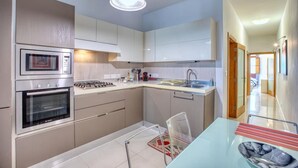 A modern kitchen with built-in appliances, a dining area with a glass table, and a view of the hallway. - Stylish St. Julian’s 1BR home, Cozy & Central! (St. Julian`s)
