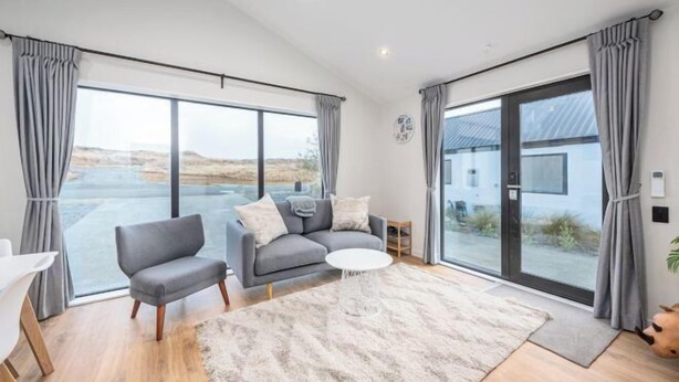 Ein geräumiges Wohnzimmer mit einem grauen Sofa, einem kleinen runden Couchtisch und einem großen Fenster mit Blick ins Freie.