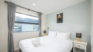 Ein Hotelzimmer mit einem großen Bett, zwei Nachttischen, einer Wandlampe und einem mit Vorhängen versehenen Fenster.