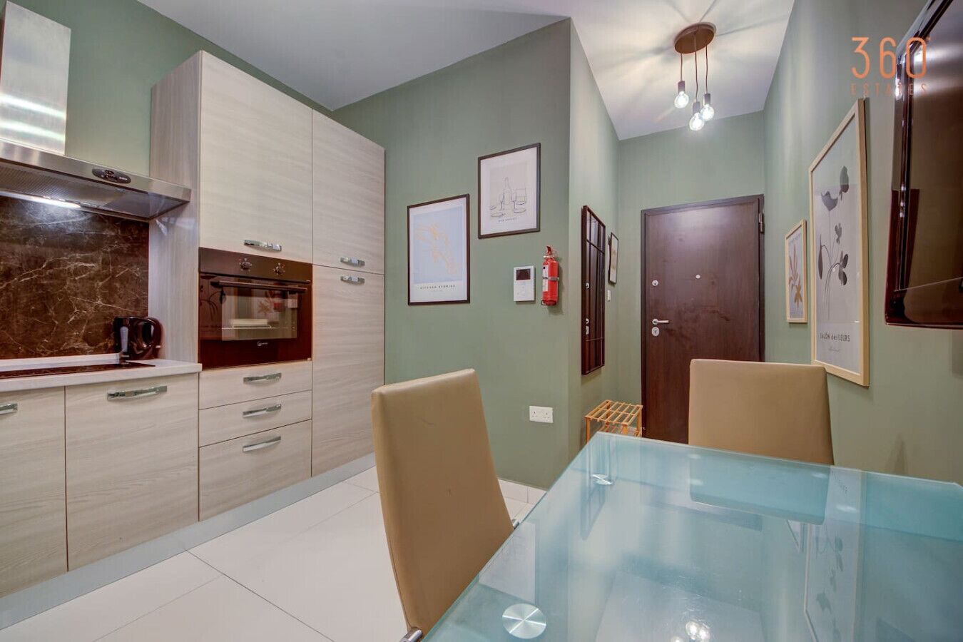 A modern kitchen with light wood cabinets, a marble countertop, and a glass dining table.