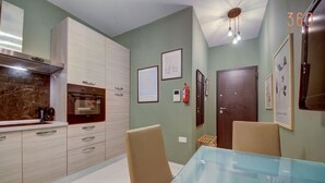 A modern kitchen with light wood cabinets, a marble countertop, and a glass dining table. - Comfortable 1BR Apt with WIFI & AC in Gzira centre (Il-Gżira)