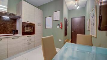 A modern kitchen with light wood cabinets, a marble countertop, and a glass dining table.
