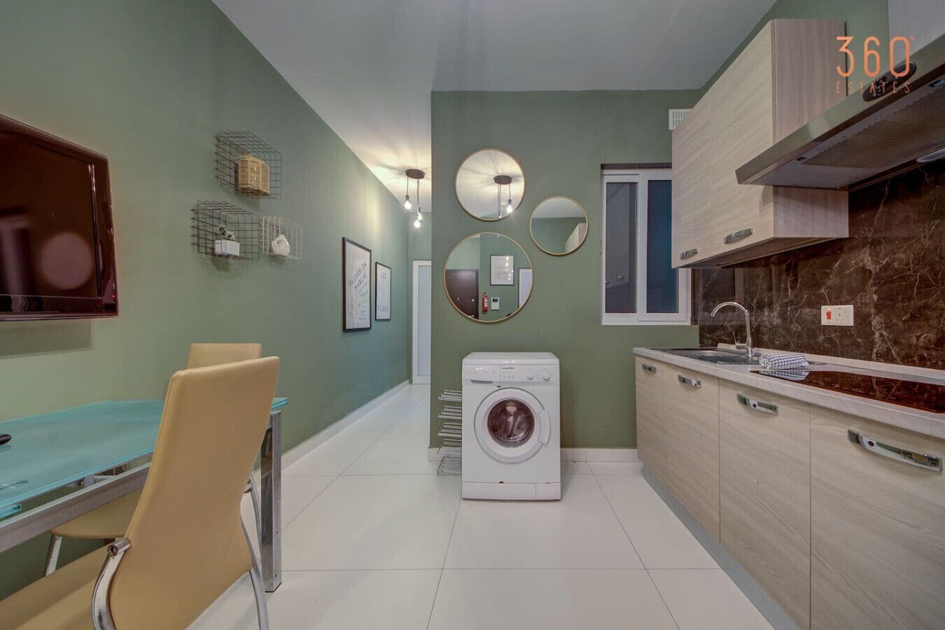 Una cocina moderna con lavadora incorporada, un comedor con mesa y sillas, y un espejo grande en la pared.