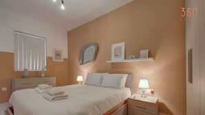 A modern bedroom with a large bed, bedside tables, a mirror, and a shelf with decorative items. - Comfortable 1BR Apt with WIFI & AC in Gzira centre (Il-Gżira)