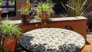 Ein Innenhof mit einem runden Tisch, Topfpflanzen und einem Gebäude mit Fliesenboden und einem Balkon.