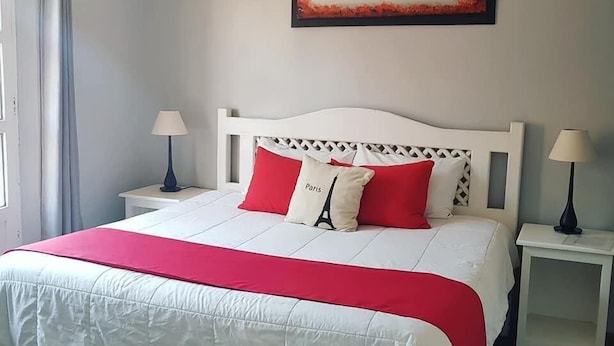 Ein Schlafzimmer mit einem weißen Bett, roten und weißen Kissen, einer roten Tagesdecke und einem Baumgemälde an der Wand.
