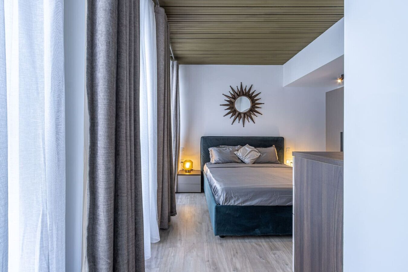 Un dormitorio moderno con una cama, una mesita de noche, un espejo en la pared y cortinas.