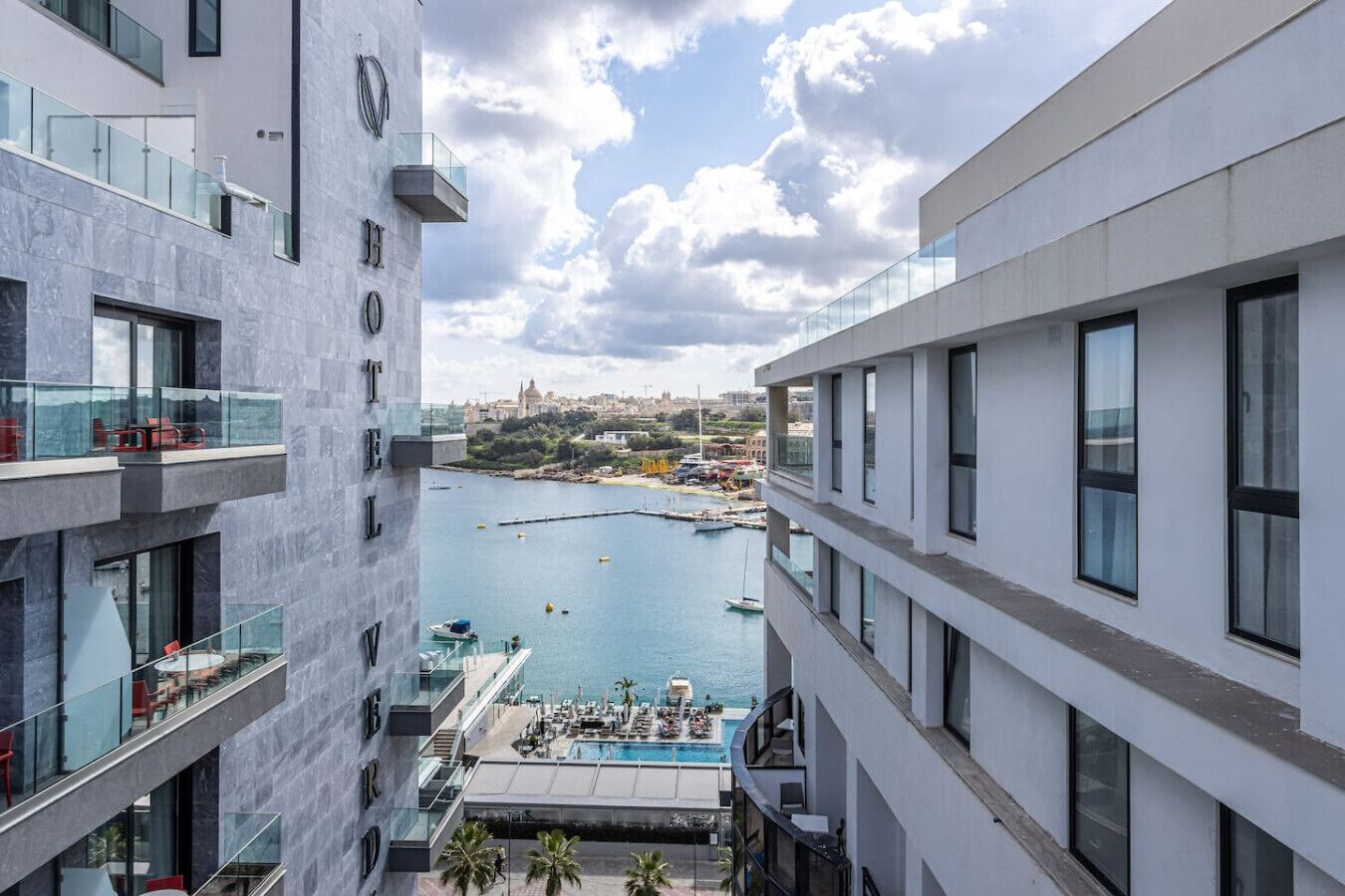 Un hotel moderno con piscina en la azotea, con vistas a un puerto deportivo y al paisaje urbano.