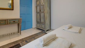 Une chambre avec une porte bleue, une armoire en bois, une table de chevet et deux serviettes enroulées.