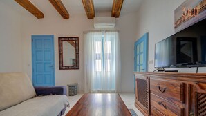 Une chambre avec un lit, une commode en bois, une télévision et une grande fenêtre avec des rideaux.
