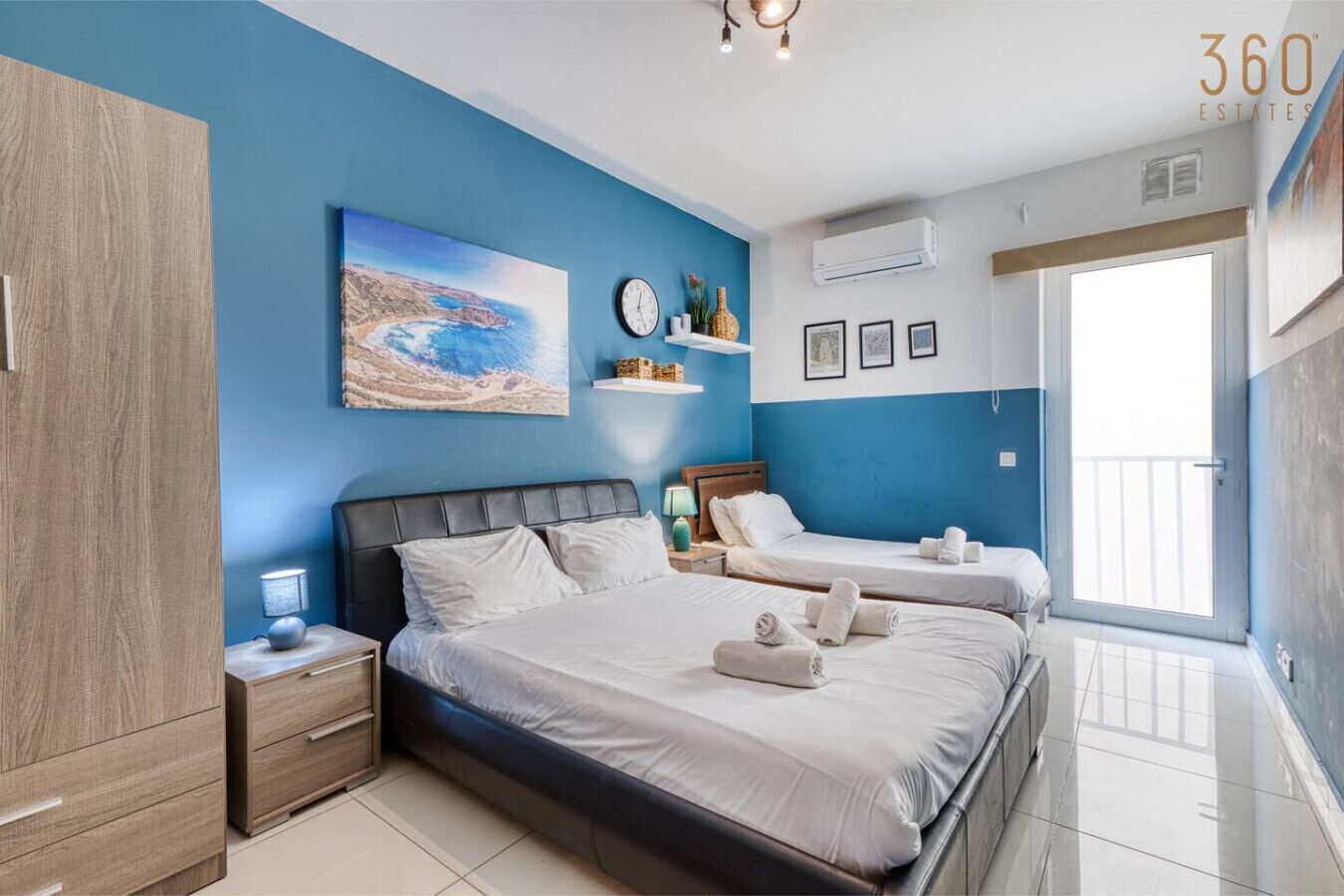 A bedroom with two beds, a wardrobe, a painting, a clock, and a window with a view.