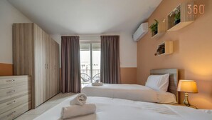 A hotel room with two beds, a dresser, a balcony, and a wall-mounted air conditioner.