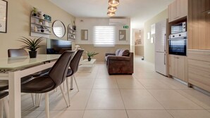 A modern kitchen with a dining area, featuring a refrigerator, oven, and a dining table with chairs.