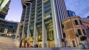A modern high-rise building with a unique architectural design, featuring a prominent entrance with steps leading up to a glass facade.