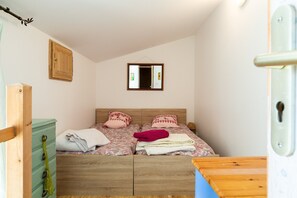 Een slaapkamer met een bed, een houten dressoir, een spiegel en een deur.