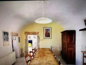 Un comedor con una larga mesa de madera, sillas, un refrigerador y obras de arte en las paredes.