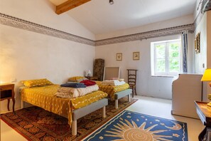 A bedroom with two beds, a window, a radiator, and a small table with a lamp.