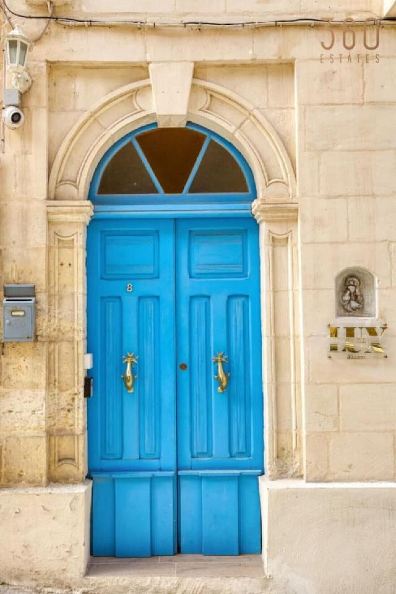Una puerta doble azul con un pequeño ventanal encima, ubicada en una fachada de edificio color beige.